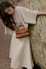 Elegant Tan Pebbled Leather Top-Handle Mini Handbag with Fold-Over Flap and Gold-Tone Hardware Styled with Neutral Knit Ensemble