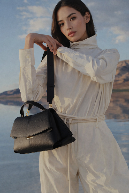 Elegant Black Pebbled Leather Top-Handle Shoulder Bag with Fold-Over Flap, Adjustable Strap, and Gold-Tone Hardware Styled in Minimalist Resort Look