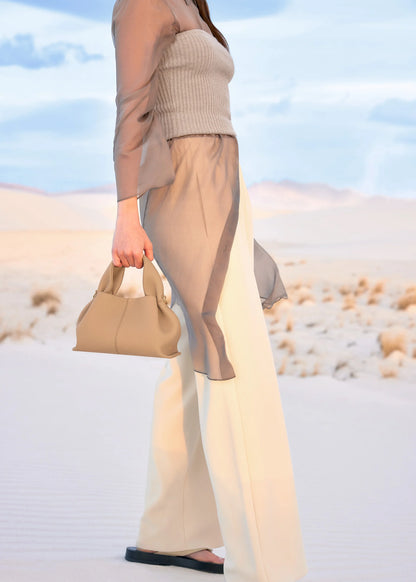 Modern Minimalist Neutral Outfit Featuring Sheer Taupe Button-Up Shirt Layered Over Ribbed Knit Bustier with Flowing Trousers and Structured Sand Beige Leather Top Handle Handbag – Elegant Contemporary Womenswear Editorial Look