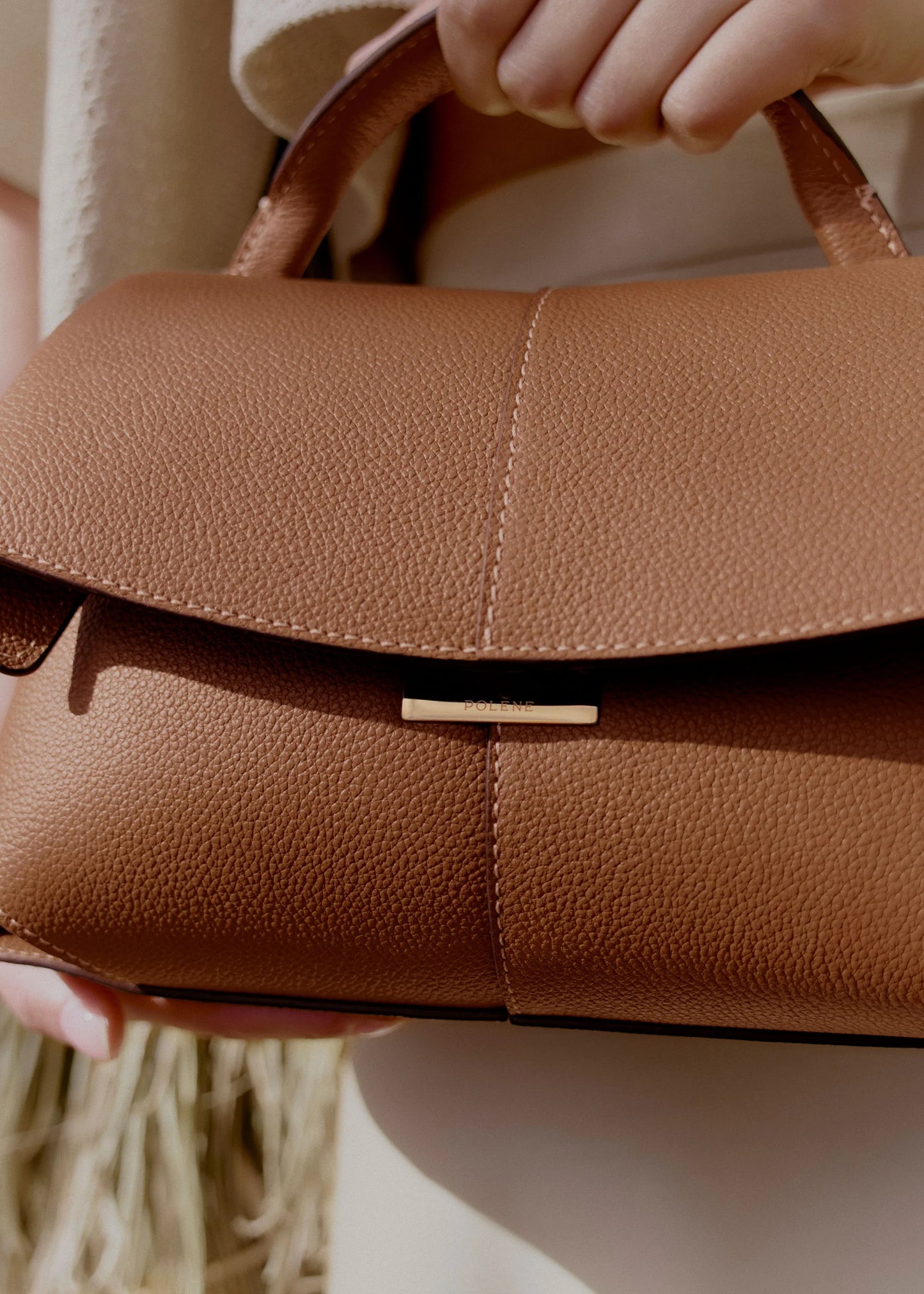 Elegant Tan Pebbled Leather Top-Handle Mini Handbag with Fold-Over Flap and Gold-Tone Hardware Styled with Neutral Knit Ensemble