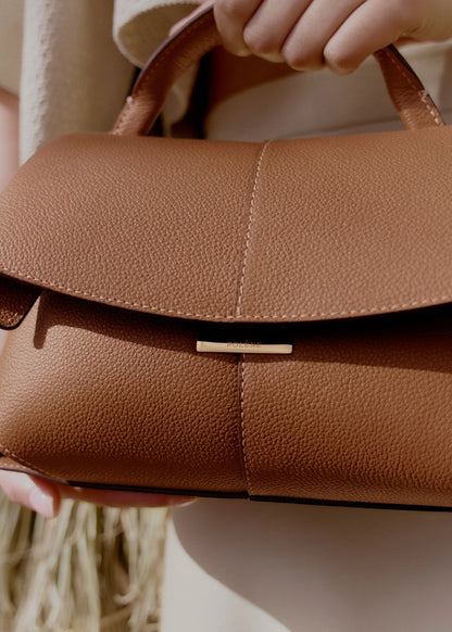Elegant Tan Pebbled Leather Top-Handle Mini Handbag with Fold-Over Flap and Gold-Tone Hardware Styled with Neutral Knit Ensemble