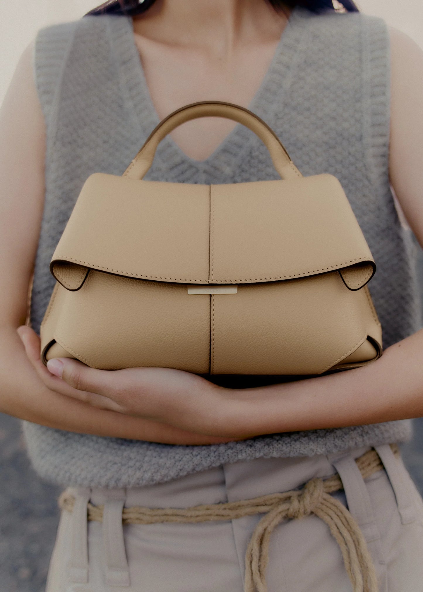 Elegant Beige Pebbled Leather Top-Handle Handbag with Fold-Over Flap and Minimalist Structured Silhouette Styled in Soft Neutral Look