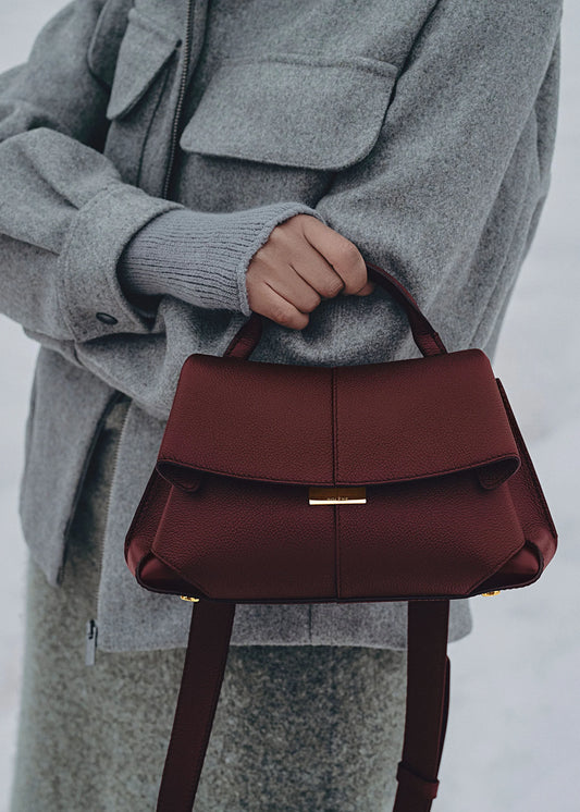 Elegant Burgundy Pebbled Leather Top-Handle Shoulder Bag with Fold-Over Flap and Gold-Tone Hardware Styled with Cozy Grey Outerwear