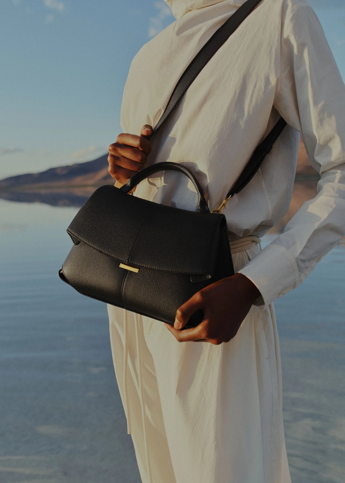 Elegant Black Pebbled Leather Top-Handle Shoulder Bag with Fold-Over Flap, Adjustable Strap, and Gold-Tone Hardware Styled in Minimalist Resort Look