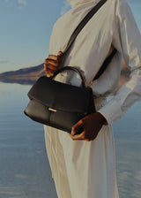 Elegant Black Pebbled Leather Top-Handle Shoulder Bag with Fold-Over Flap, Adjustable Strap, and Gold-Tone Hardware Styled in Minimalist Resort Look